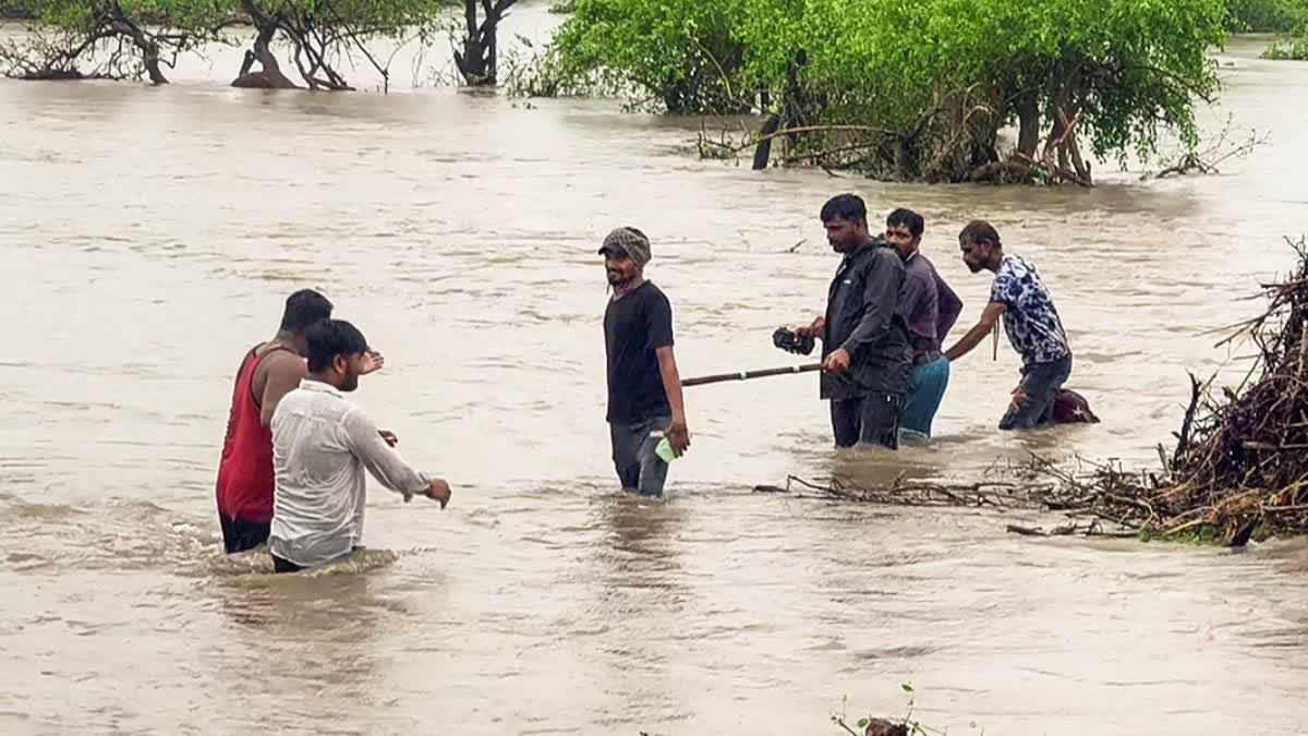 Villagers wade through flood water after heavy rainfall in Surendranagar on June 24