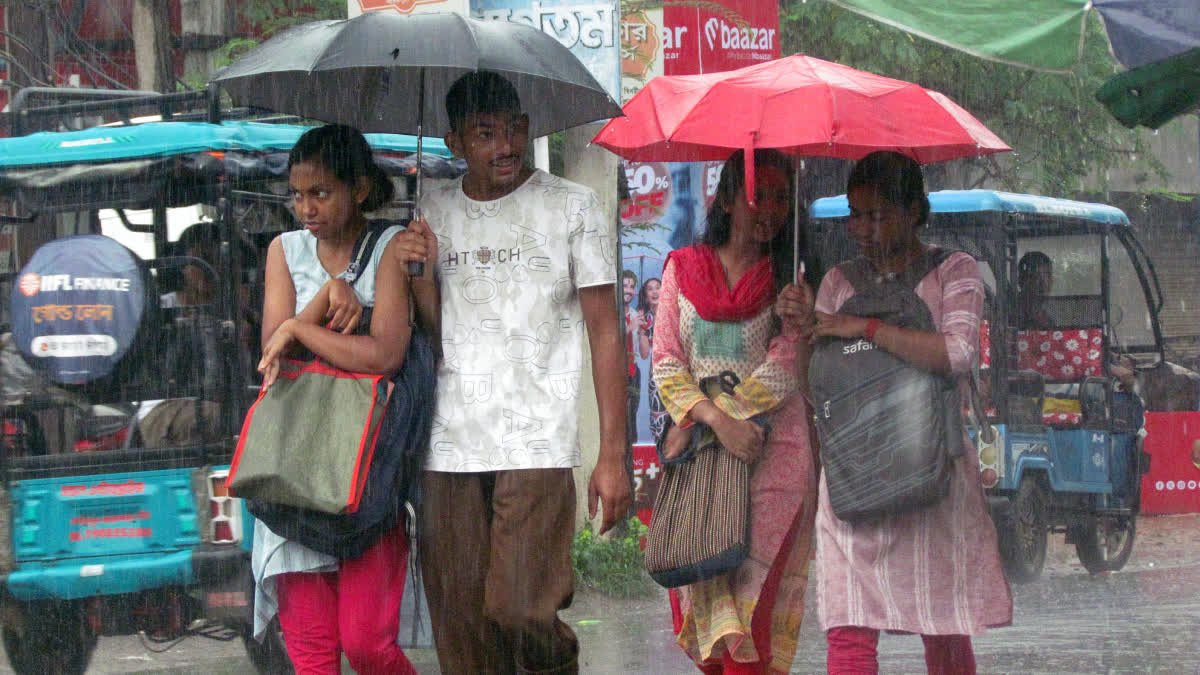 नादिया में बारिश के बीच सड़क पर छाते लेकर चलते लोग।