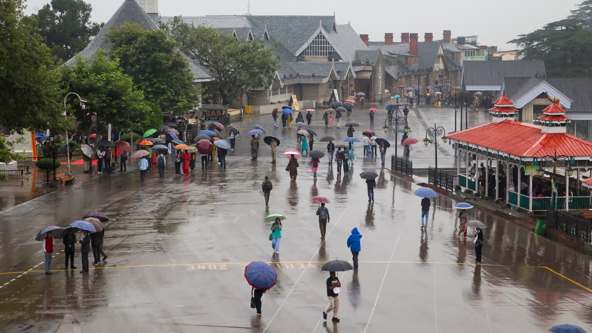People walk with umbrellas across the Ridge Maidan amid rain in Shimla, Himachal Pradesh, on Tuesday.